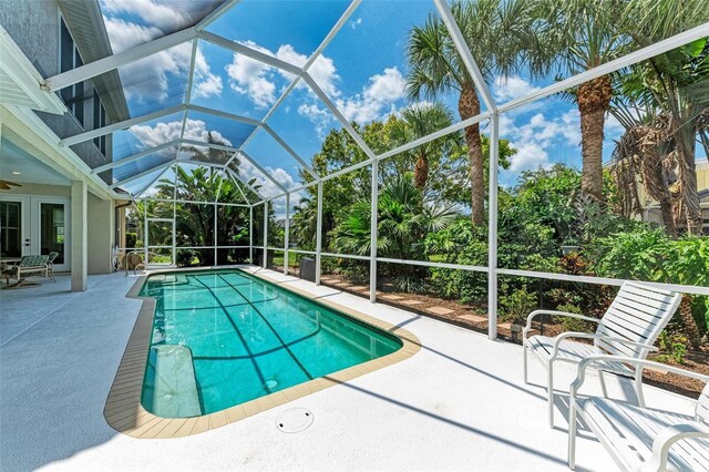 view of swimming pool with ceiling fan, glass enclosure, and a patio area