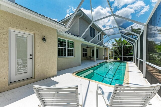 view of pool with ceiling fan, glass enclosure, and a patio area