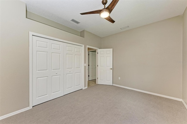 unfurnished bedroom featuring a closet, light colored carpet, a textured ceiling, and ceiling fan