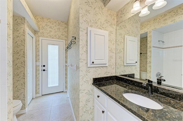 bathroom with tiled shower, tile patterned flooring, toilet, and vanity