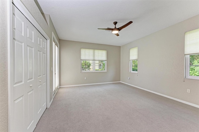 unfurnished bedroom featuring multiple windows, a closet, light colored carpet, and ceiling fan