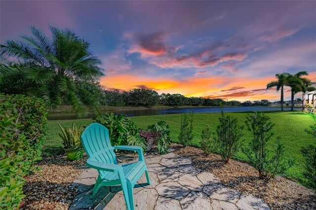 patio terrace at dusk featuring a yard and a water view