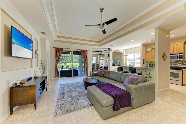 tiled living room with a raised ceiling, ceiling fan, and crown molding