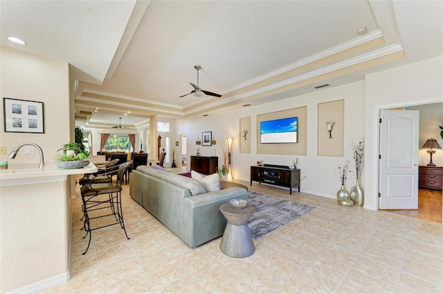 tiled living room with ceiling fan, a tray ceiling, and crown molding