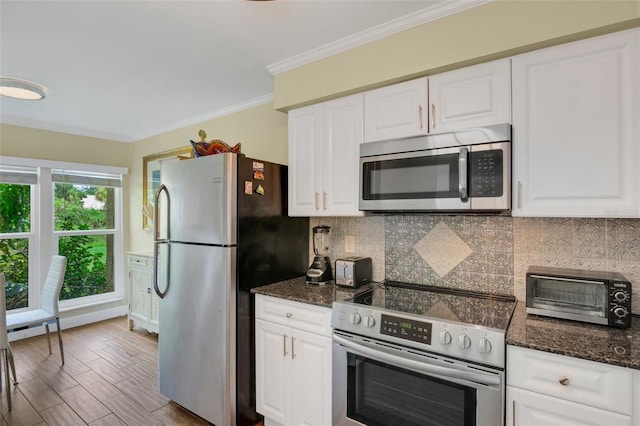 kitchen with appliances with stainless steel finishes, white cabinetry, ornamental molding, dark stone counters, and light hardwood / wood-style flooring