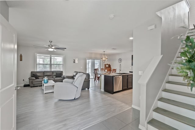 living area featuring light wood-type flooring, ceiling fan with notable chandelier, baseboards, and stairs