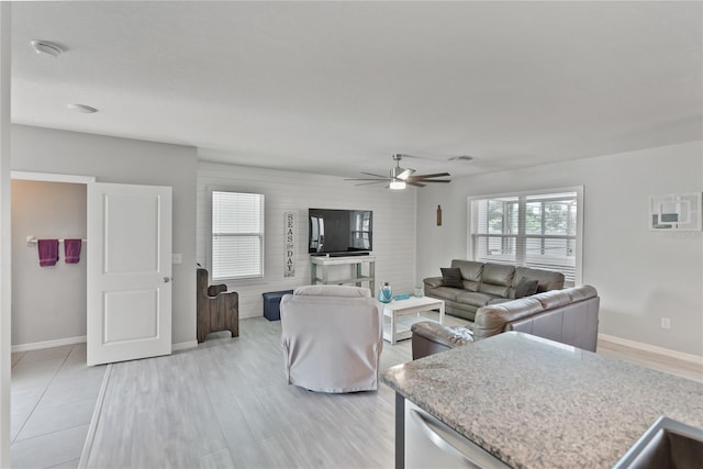 living area featuring light wood-style floors, baseboards, and a ceiling fan