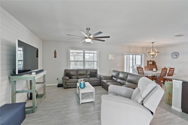 living room with wood walls, visible vents, baseboards, light wood-type flooring, and an inviting chandelier