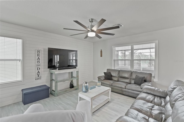 living area with light wood finished floors, a ceiling fan, and wooden walls