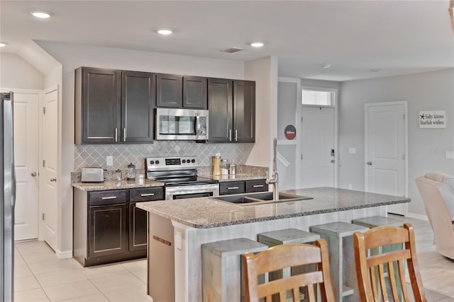 kitchen featuring light stone counters, visible vents, appliances with stainless steel finishes, an island with sink, and a kitchen bar