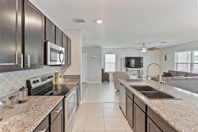 kitchen featuring stainless steel appliances, a sink, open floor plan, light stone countertops, and tasteful backsplash