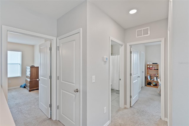 corridor featuring baseboards, visible vents, and light colored carpet