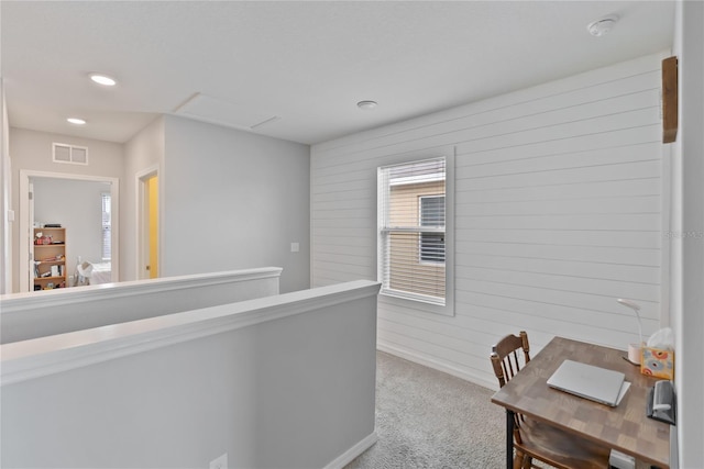 hallway featuring carpet floors, recessed lighting, visible vents, wood walls, and an upstairs landing