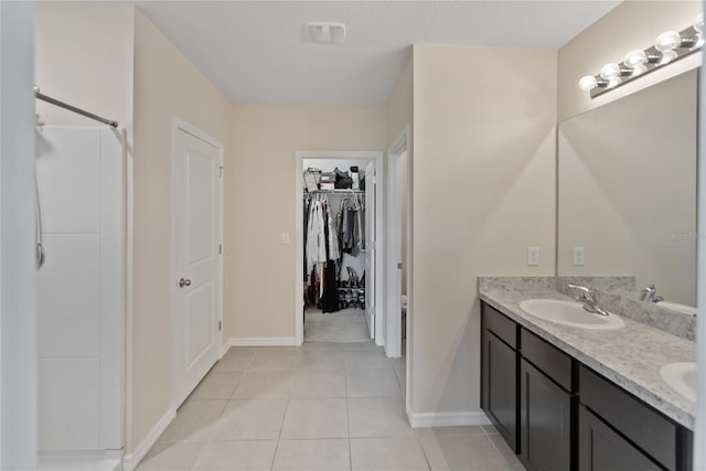 full bathroom featuring a sink, baseboards, tile patterned floors, double vanity, and a walk in closet