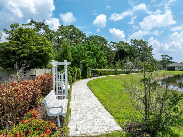 surrounding community with a water view, fence, and a lawn