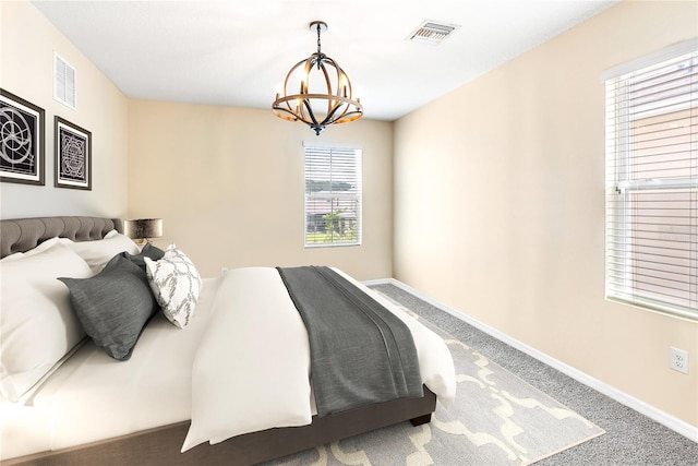 carpeted bedroom with an inviting chandelier, baseboards, and visible vents