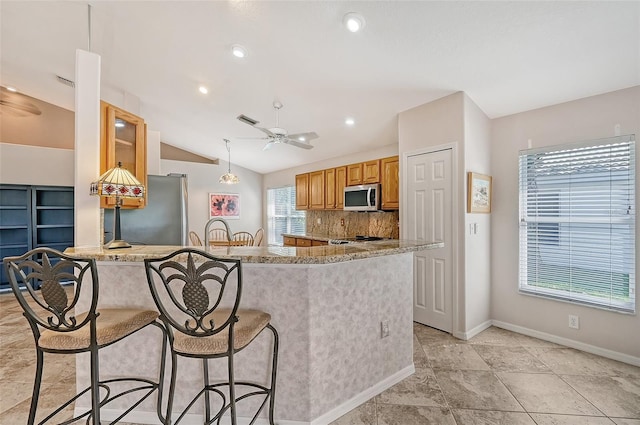 kitchen featuring kitchen peninsula, appliances with stainless steel finishes, decorative backsplash, light stone counters, and vaulted ceiling