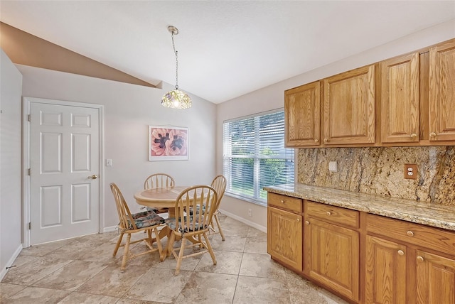 kitchen with light stone countertops, backsplash, pendant lighting, lofted ceiling, and light tile patterned floors