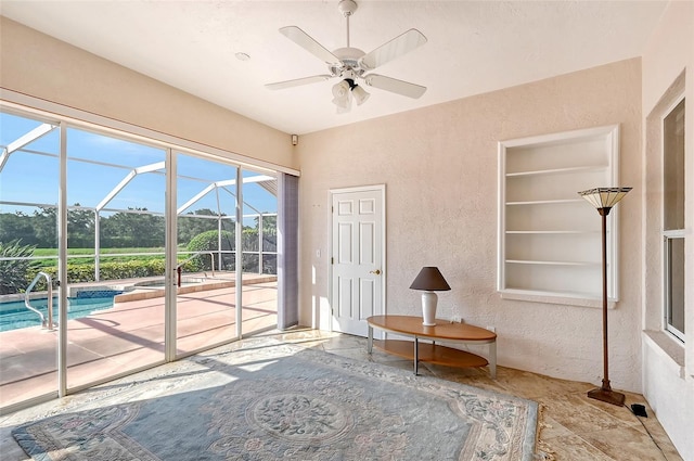 unfurnished room with built in shelves, ceiling fan, a pool, and a wealth of natural light