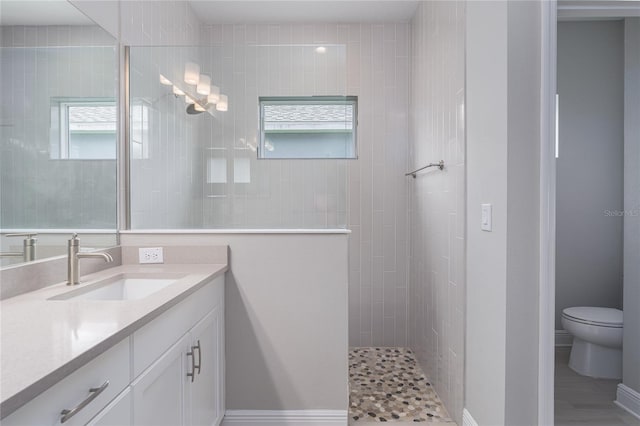 bathroom featuring a tile shower, vanity, and toilet