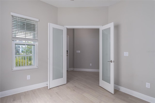 spare room with french doors, light wood-type flooring, and vaulted ceiling