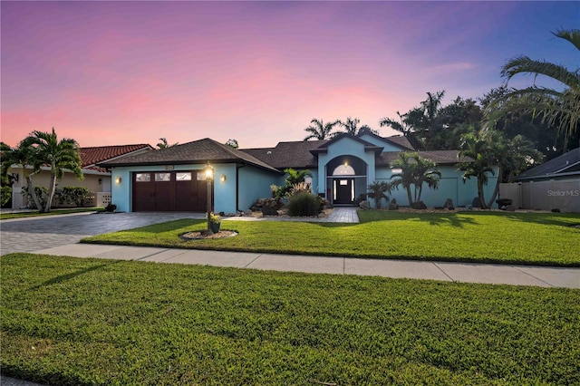 view of front facade featuring an attached garage, stucco siding, decorative driveway, and a yard