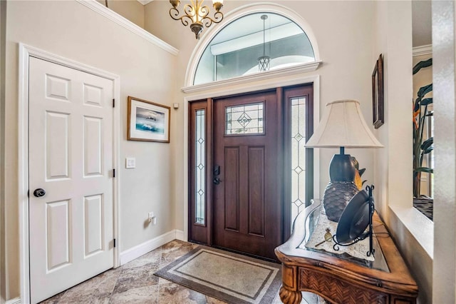 foyer with a notable chandelier, a high ceiling, ornamental molding, stone finish floor, and baseboards