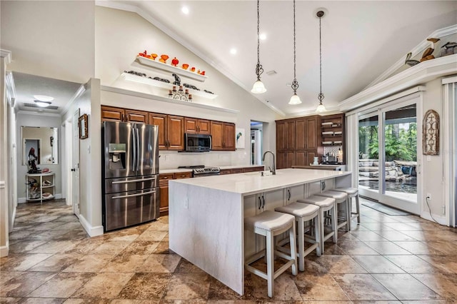 kitchen featuring an island with sink, hanging light fixtures, ornamental molding, appliances with stainless steel finishes, and a breakfast bar area