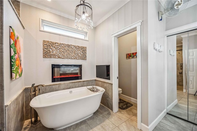 bathroom featuring toilet, ornamental molding, wainscoting, a soaking tub, and a glass covered fireplace