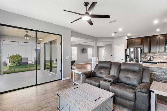 living room with sink, a textured ceiling, ceiling fan, and light wood-type flooring