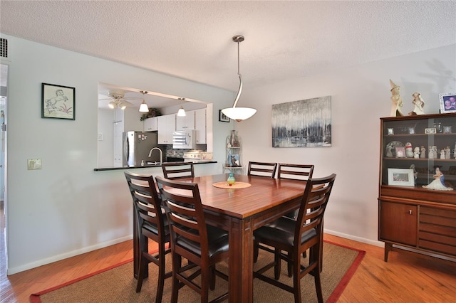 dining room with a textured ceiling, light wood-type flooring, and ceiling fan