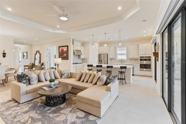 living room featuring sink, ceiling fan, ornamental molding, a tray ceiling, and light tile patterned flooring