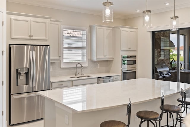 kitchen featuring appliances with stainless steel finishes, sink, white cabinets, a kitchen island, and hanging light fixtures