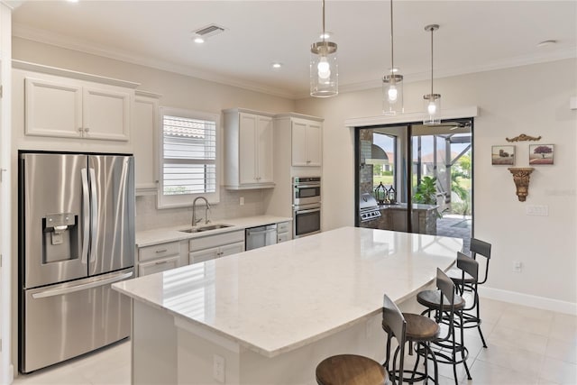 kitchen with pendant lighting, sink, appliances with stainless steel finishes, a kitchen island, and white cabinetry