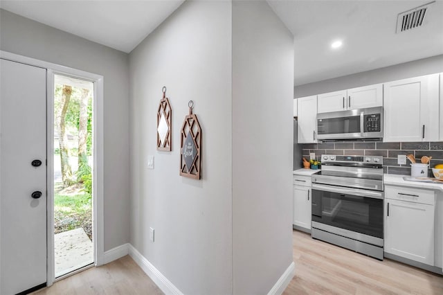 kitchen with appliances with stainless steel finishes, white cabinets, decorative backsplash, and light hardwood / wood-style floors