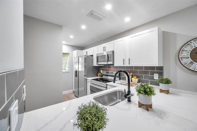 kitchen with decorative backsplash, appliances with stainless steel finishes, white cabinetry, light hardwood / wood-style floors, and light stone counters