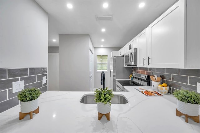 kitchen featuring stainless steel appliances, light stone countertops, white cabinets, sink, and tasteful backsplash