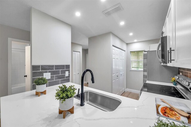 kitchen with light stone counters, white cabinetry, electric range oven, tasteful backsplash, and sink