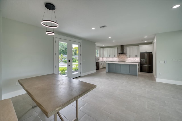 kitchen with decorative backsplash, wall chimney range hood, french doors, stainless steel fridge, and a kitchen island