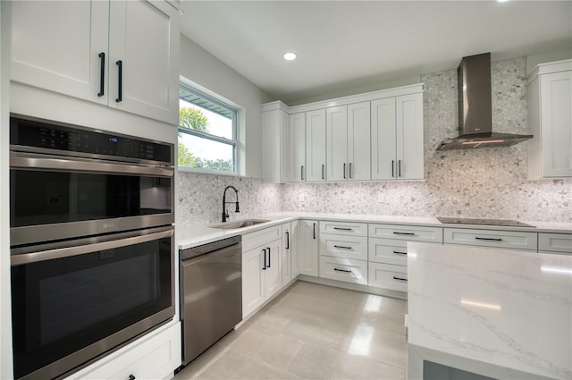 kitchen featuring appliances with stainless steel finishes, white cabinetry, backsplash, sink, and wall chimney range hood