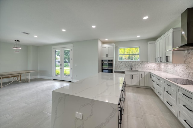 kitchen featuring stainless steel double oven, light stone countertops, wall chimney exhaust hood, light tile patterned floors, and tasteful backsplash