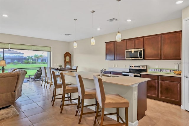 kitchen with light tile patterned flooring, stainless steel appliances, decorative light fixtures, and an island with sink