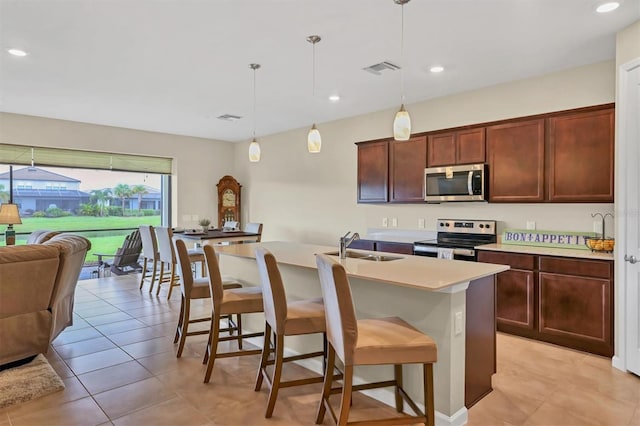 kitchen with hanging light fixtures, a breakfast bar area, stainless steel appliances, sink, and a kitchen island with sink