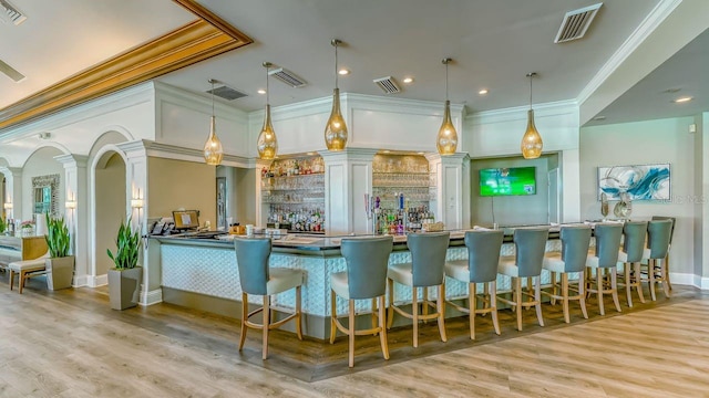 bar with ornate columns, ornamental molding, pendant lighting, and light wood-type flooring