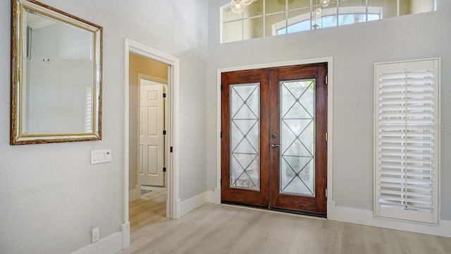 foyer featuring light hardwood / wood-style floors, a high ceiling, and french doors