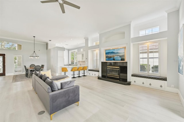 living room featuring light wood-type flooring, ceiling fan with notable chandelier, crown molding, and sink