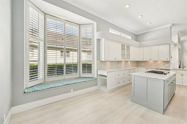 kitchen with tasteful backsplash, ornamental molding, sink, white cabinets, and a kitchen island