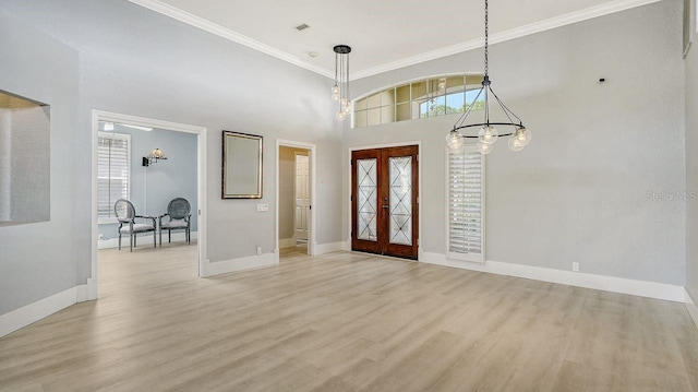 foyer entrance featuring crown molding, a towering ceiling, an inviting chandelier, and light hardwood / wood-style flooring