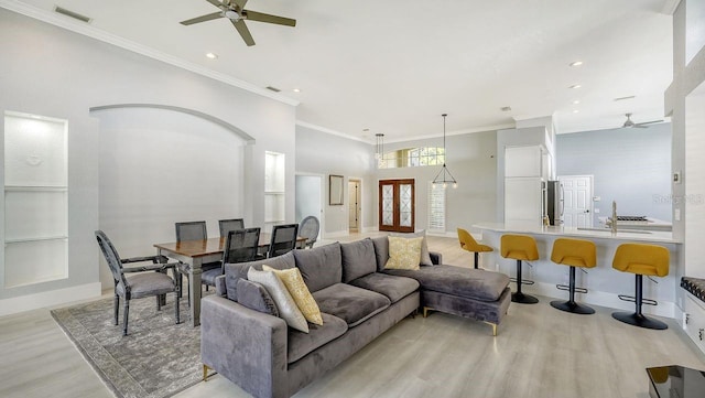 living room with sink, ceiling fan, a towering ceiling, ornamental molding, and light wood-type flooring