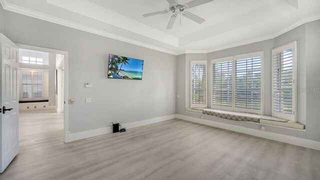 empty room with a tray ceiling, light hardwood / wood-style flooring, ornamental molding, and ceiling fan